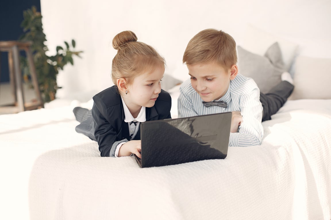 Little children using laptop together lying on bed